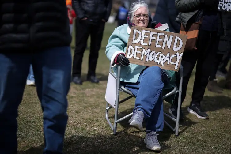 79-year-old Christine Hughes holds a sign as she attends a demonstration during the day of 
